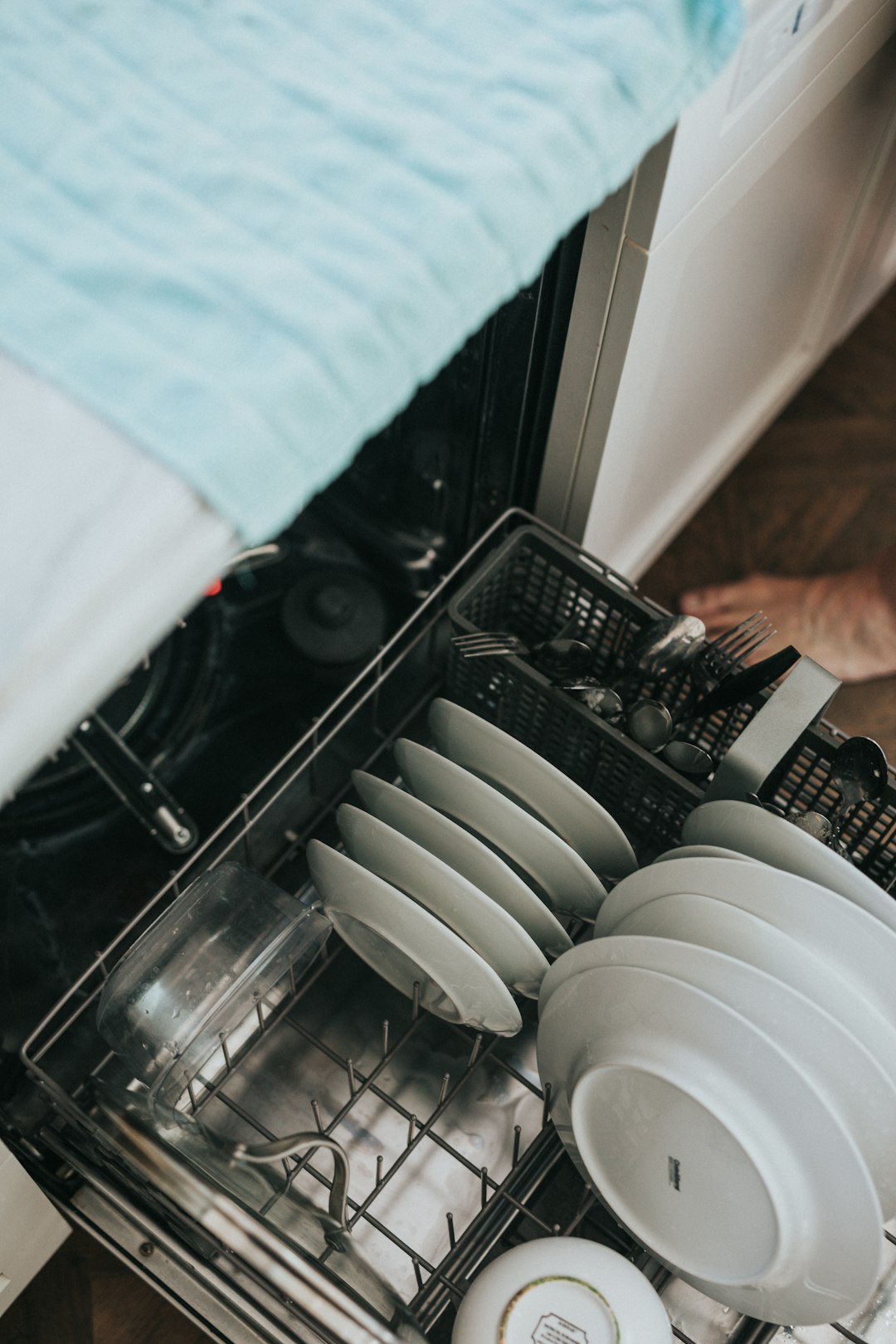 Open dishwasher with plates and cutlery in its lower rack