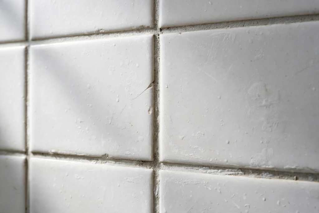 Close-up of white ceramic shower tiles with light soap scum buildup and water droplets